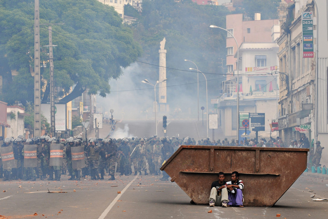 © Walter Astrada / Agence France-Presse # 019 Deux partisans d'Andry Rajoelina, maire d'Antananarivo, se tenant derrière une benne, à l'abri des tirs de gaz lacrymogène des forces de l'ordre. Antananarivo, 16 février 2009.