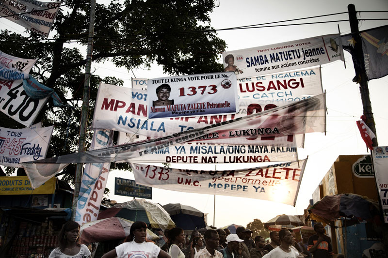 Banderoles de candidats députés cote à cote au-dessus d’un marché populaire à Kinshasa. © Joseph Moura